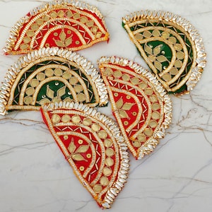 以下が含まれることがあります： 赤と緑の背景に金色の刺繍、スパンコール、小さな葉の形をした鏡があしらわれた、5つの半円形の布製パッチ。各パッチの縁には、小さく尖った反射性の装飾が施されています。