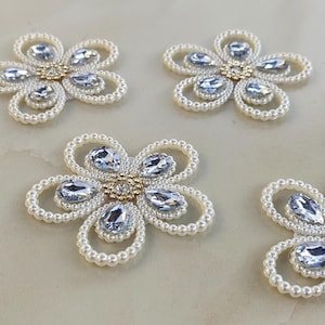 May include: Four flower-shaped embellishments featuring a central cluster of small gold-toned beads and clear crystals. Each petal is outlined with white faux pearls and contains a single teardrop-shaped clear crystal at its center.