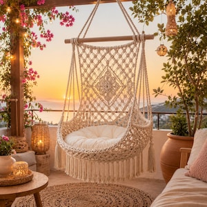 May include: A cream-coloured macrame hanging chair featuring an intricate knotted diamond pattern, a wooden spreader bar, and long fringe tassels. The chair includes a plush, round off-white cushion and is suspended by thick woven cotton ropes.
