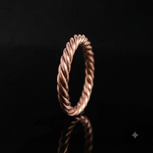 Könnte beinhalten: Ein Ring aus Roségold mit einem durchgehenden gedrehten Seildesign. Das Band hat eine polierte metallische Oberfläche mit einer sich wiederholenden diagonalen Textur, die ein spiralförmiges Aussehen um den gesamten Umfang des Schmuckstücks erzeugt.