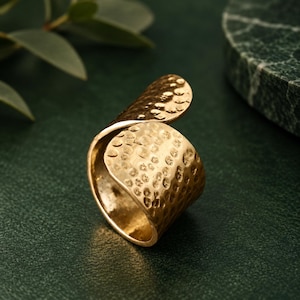 Peut inclure: Une bague dorée dotée d'une large bande ouverte avec une surface martelée et texturée. Le métal se courbe en un design superposé et chevauchant, créant une forme fluide et continue qui capte la lumière sur son extérieur alvéolé.