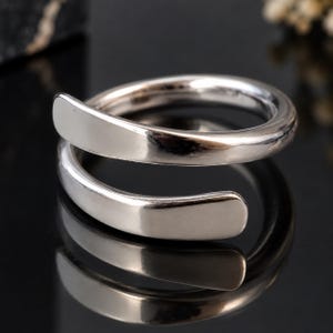 Peut inclure: Une bague bypass en métal argenté poli dotée d'un anneau lisse et continu qui s'enroule sur lui-même en spirale. La bague présente une finition réfléchissante très brillante avec des extrémités arrondies et effilées, offrant un aspect épuré.