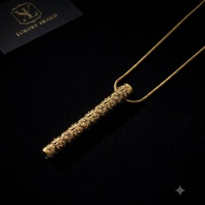 Può includere: Una collana con pendente cilindrico color oro caratterizzata da un motivo floreale ripetuto lungo tutta la lunghezza del tubo. Il pendente è appeso a una sottile catenina color oro abbinata. Un piccolo cartoncino nero con la scritta LUXURY BRAND.