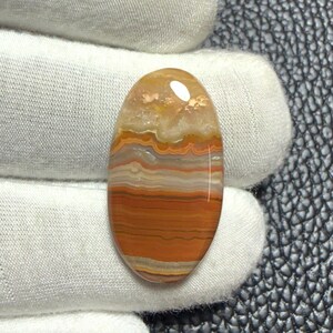 Könnte beinhalten: Ein ovaler Cabochon-Edelstein mit horizontalen Farbbändern in den Tönen gebranntes Orange, Creme, Weiß und durchscheinendem Hellbraun. Der Stein hat eine glatte, polierte Oberfläche mit einem reflektierenden Glanzlicht an der Oberseite.