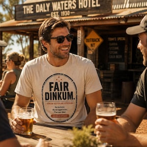 Könnte beinhalten: Ein cremefarbenes Kurzarm-T-Shirt mit einem kreisförmigen Aufdruck mit dem Text FAIR DINKUM. GENUINE AUSTRALIAN EXPRESSION. No bullshit. No exaggeration. The real deal. AUSTRALIAN APPROVED. Das T-Shirt wird von einer Person mit dunklem Haar getragen.
