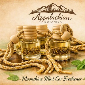 May include: Four small glass bottles filled with golden liquid and dried herbs, each topped with a ribbed wooden cap and a braided rope for hanging. The text Appalachian Botanica and Moonshine Mint Car Freshener is visible.