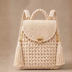 Puede incluir: Una mochila de ganchillo en color beige con un patrón de punto texturizado, un asa superior y dos correas ajustables. La solapa frontal se asegura con un cierre de metal dorado y está decorada con dos largas borlas de hilo beige a los lados.