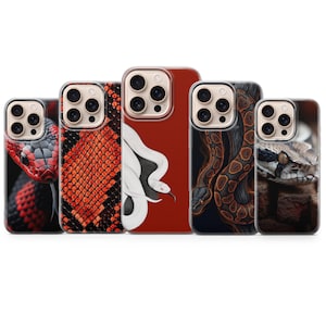 Puede incluir: Cinco fundas para smartphone con diversos diseños de serpientes. Las fundas muestran patrones de escamas rojas y negras, una serpiente blanca sobre fondo rojo sólido, una serpiente marrón enroscada sobre fondo oscuro y un primer plano de cabeza.