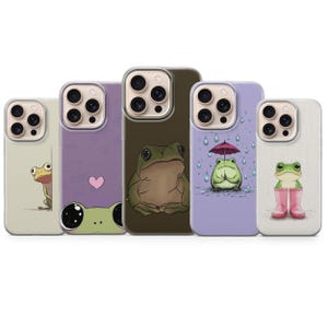 Puede incluir: Cinco fundas para smartphone con diversas ilustraciones de ranas. Una funda muestra una rana asomándose, otra tiene una rana con un corazón rosa, una tercera muestra una rana grande, una cuarta una rana con paraguas bajo la lluvia y otra en botas.