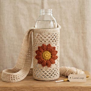 May include: A beige crochet water bottle holder featuring a lattice pattern and a large, three-dimensional flower motif in rust orange and yellow. The holder includes a long, matching crochet strap and a small tag labeled LunaLoop.