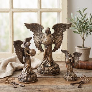 May include: Three bronze-colored angel figurines of varying heights, each featuring detailed wings and flowing robes. Each angel stands on a textured base resembling clouds and holds a spherical object with geometric patterns in their hands.