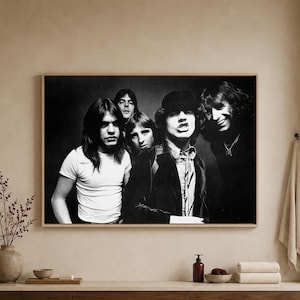 Könnte beinhalten: Ein rechteckiger Wandkunstdruck mit einem Schwarz-Weiß-Foto der Rockband AC/DC. Das Bild zeigt vier Bandmitglieder in einem Gruppenporträt, wobei ein Mitglied eine Mütze und eine Krawatte trägt, gerahmt in einem hellen Holzrahmen.