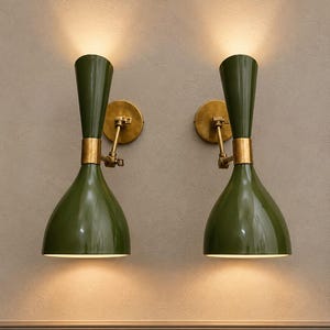 Peut inclure: Deux appliques murales dotées d'abat-jours en métal vert olive en forme de sablier avec une finition brillante. Chaque lampe possède une fixation murale circulaire en laiton et un bras articulé réglable diffusant une lumière chaude.