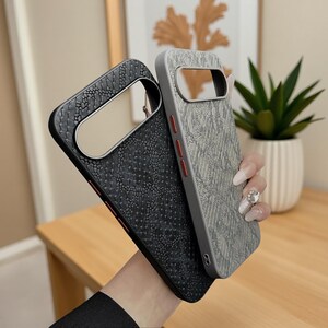 Op de afbeelding: Twee beschermende telefoonhoesjes met een gestructureerd slangenleerpatroon. De ene hoes is zwart en de andere is lichtgrijs. Beide hoesjes hebben een grote horizontale uitsparing voor de cameramodule en opvallende rode knoppen aan de zijkant.