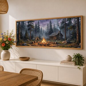 May include: A panoramic landscape painting in a wooden frame depicting a rustic log cabin and a small tent nestled in a dense pine forest at twilight, with a bright orange campfire burning in the center, surrounded by tall trees and rocky terrain.