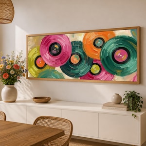 May include: A rectangular wall art piece featuring an abstract oil painting of overlapping vinyl records in vibrant shades of pink, green, orange, and yellow. The artwork is enclosed in a thin, light-colored wooden frame and displays thick, textured brushstrokes throughout the composition.