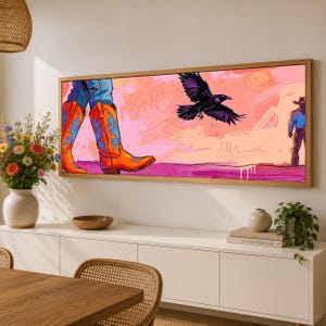 May include: A rectangular framed wall art print featuring a vibrant illustration of orange cowboy boots with blue flame patterns, a black crow in flight, and a silhouette of a person in a hat against a pink and peach desert-toned background.