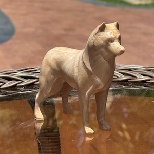 May include: A light brown wooden figurine carved in the shape of a standing wolf. The sculpture features detailed facial features, pointed ears, and a smooth, natural wood grain texture throughout the entire body of the animal figure.