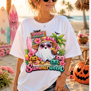 May include: A white t-shirt featuring a graphic of a ghost wearing a straw hat and heart-shaped sunglasses, holding a coconut drink. The design includes a pink surfboard, palm trees, pumpkins, and the text "SPOOKY BEACH CLUB" and "Summerween".