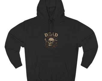 May include: A black hooded sweatshirt featuring a graphic on the chest with the text DEAD INSIDE. The design includes a central human skull surrounded by small floral elements, a crescent moon, and flying bats in muted beige and orange tones.