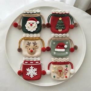 May include: Six small crochet drawstring pouches featuring holiday designs including a Santa Claus, a Christmas tree, a reindeer, a Santa hat, a white snowflake, and a gingerbread man, each with scalloped edges and pom-pom drawstring ends.