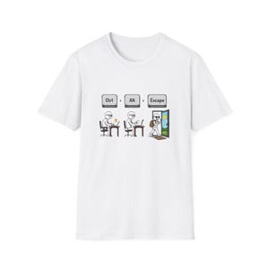 May include: A white short-sleeved t-shirt featuring a graphic print of three stick figures. The design shows the text Ctrl, Alt, and Escape above figures working at desks, with the final figure walking out a door into a sunny landscape.