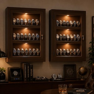 May include: Two dark brown rectangular wall-mounted display cases with glass doors, each featuring three illuminated shelves holding rows of various wristwatches. Below, a watch winder, books titled Rolex and Patek Philippe, and a globe.