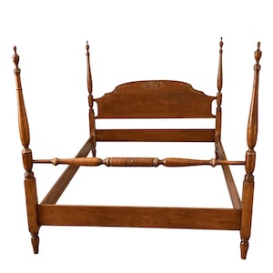 May include: A four-poster bed frame crafted from medium-toned wood, featuring tall, slender posts with decorative finials at the top. The headboard is arched with a central floral motif, and the frame includes side rails and a footboard rail.