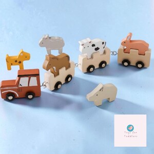 May include: A wooden toy train set featuring a brown engine and three connected carriages carrying a brown horse, a white and black spotted cow, and an orange rabbit. A yellow dog and a light grey animal figure are placed separately nearby.