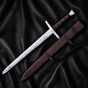 May include: A double-edged sword with a patterned silver-toned blade, a straight crossguard, and a dark brown leather-wrapped grip with a metallic pommel. Beside the sword lies a matching dark brown leather scabbard with black leather accents.