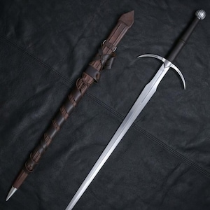 Peut inclure: Une épée en acier avec une poignée sombre et un pommeau arrondi, dotée d'une garde en argent aux quillons incurvés. À côté se trouve un fourreau en cuir marron enveloppé de lanières assorties, se terminant par une pointe métallique.