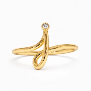 May include: A gold ring featuring a continuous, fluid band that curves into an open, looping design. At the top of the vertical curve, a single, small, round, clear gemstone is set in a bezel, providing a focal point to the polished metal.