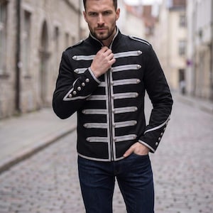 May include: A black military-style jacket featuring a high collar, silver-toned braided trim across the chest, and silver buttons. The jacket includes shoulder epaulets and decorative silver trim on the cuffs, paired with dark blue denim jeans.