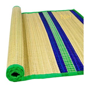 Puede incluir: Una esterilla tejida con una base de color tostado natural y rayas verticales prominentes en azul y verde vibrantes. La esterilla está parcialmente enrollada en un extremo y rematada con un borde de tela verde brillante. Se ven las letras TGH.