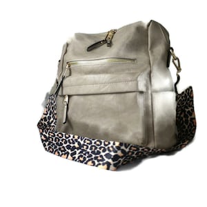 May include: A grey faux leather tote bag with a black and orange leopard print strap. The bag has a zip closure and a front pocket.