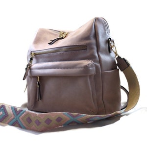 May include: A light pink leather backpack with a gold zipper and a patterned strap. The strap is beige with blue, pink, and purple geometric designs.