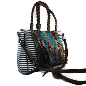 May include: A striped and patterned tote bag with brown braided handles and a long strap. The bag has a colorful geometric pattern on one side and white and black stripes on the other side.