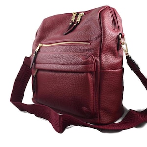 May include: A burgundy leather shoulder bag with multiple zippered compartments and a front pocket. The bag features gold-toned zippers and hardware, and a matching burgundy adjustable shoulder strap.