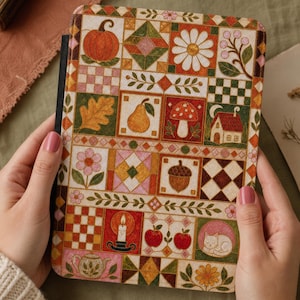 May include: A rectangular e-reader case featuring a colorful patchwork quilt design. The pattern includes illustrations of a pumpkin, daisy, pear, mushroom, house, acorn, candle, apples, cat, and teapot, arranged in a grid with checkered borders.