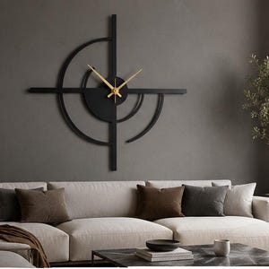 Peut inclure: Une grande horloge murale noire au design géométrique composé de lignes entrecroisées et d'arcs de cercle. L'horloge présente un moyeu central circulaire avec de fines aiguilles dorées pour les heures, les minutes et les secondes en métal.