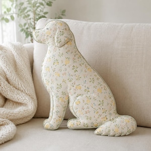 May include: A dog-shaped scatter cushion featuring a cream-coloured fabric with a delicate floral pattern of small yellow lemons, green leaves, and tiny blue flowers. The cushion is shaped like a sitting dog with a defined head, ears, and tail.