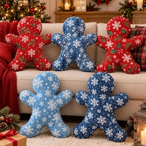 May include: Five gingerbread man-shaped pillows featuring festive holiday patterns. Three pillows display red fabric with white snowflakes and green holly, while two pillows feature blue fabric with white snowflakes and small pine tree motifs.