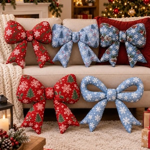 Könnte beinhalten: Fünf schleifenförmige Dekokissen mit festlichen Weihnachtsmustern. Zwei Kissen sind rot mit weißen Schneeflocken und grünen Tannen, zwei sind hellblau mit weißen Schneeflocken und Tannen, eines ist blau mit Tannenzapfen und Schneeflocken.