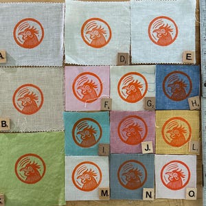 May include: A collection of fabric squares in various colors, each featuring a circular orange rooster design. The squares are arranged on a surface with a measuring tape along the right side. The fabric colors include light gray, pink, blue, and yellow.
