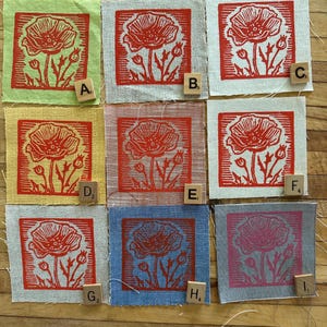May include: Nine fabric squares with a red poppy design, each on a different colored background. The squares are arranged in a 3x3 grid. Scrabble tiles with letters A through I are placed near each square.