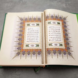 May include: An open book with a green cover featuring intricate Arabic calligraphy on cream-colored pages. The text is framed by elaborate, colorful geometric and floral borders in shades of gold, blue, and orange, with radiating line patterns.