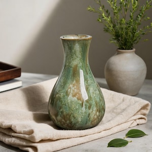 Könnte beinhalten: Eine Keramikvase mit bauchigem Körper und engem Hals, die eine glänzende Glasur in Salbeigrün, Waldgrün und Erdbraun mit weißen Sprenkeln aufweist und eine durchgehend glatte, reflektierende Oberfläche besitzt.