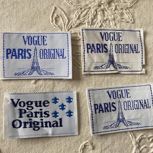May include: Four white fabric labels with blue text and borders. The labels read "VOGUE PARIS ORIGINAL" with an Eiffel Tower illustration. One label features fleur-de-lis symbols.