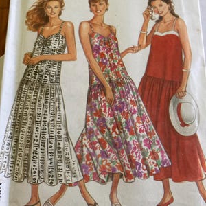 May include: A sewing pattern envelope featuring illustrations of three variations of a sleeveless maxi dress with thin straps. One dress has a black and white geometric print, one has a colorful floral pattern, and one is solid red with a white bodice trim.