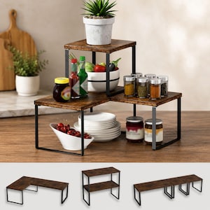 May include: A tiered corner shelf organizer featuring dark brown wood-grain surfaces and black metal frames. The unit is displayed with various kitchen items including spice jars, a white bowl with cherries, a stack of plates, and a potted plant.